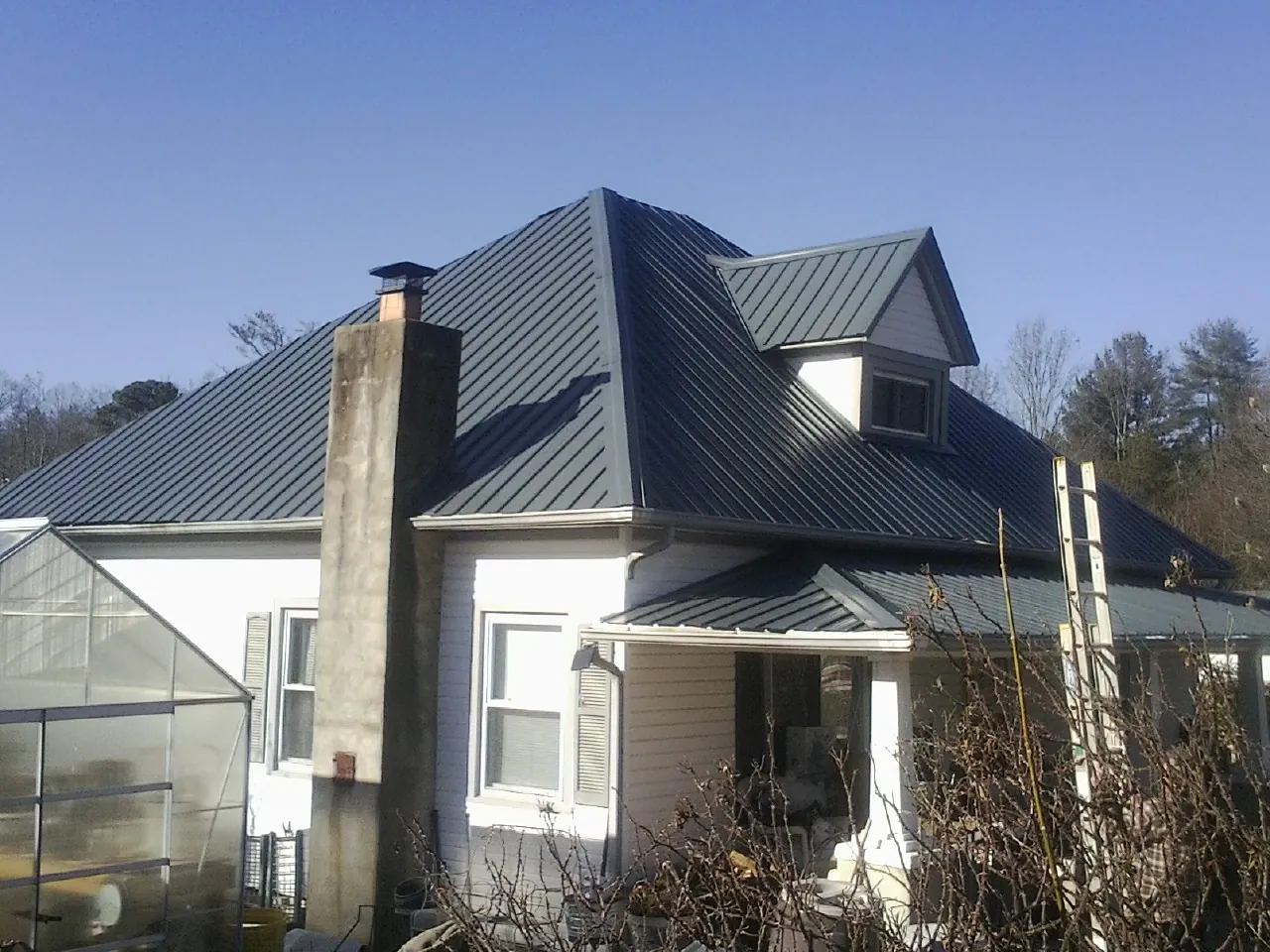 Dark blue standing seam metal roof on a white farmhouse with dormer — Slate & Tile Roof Repair by Roofing Brothers in Horatio