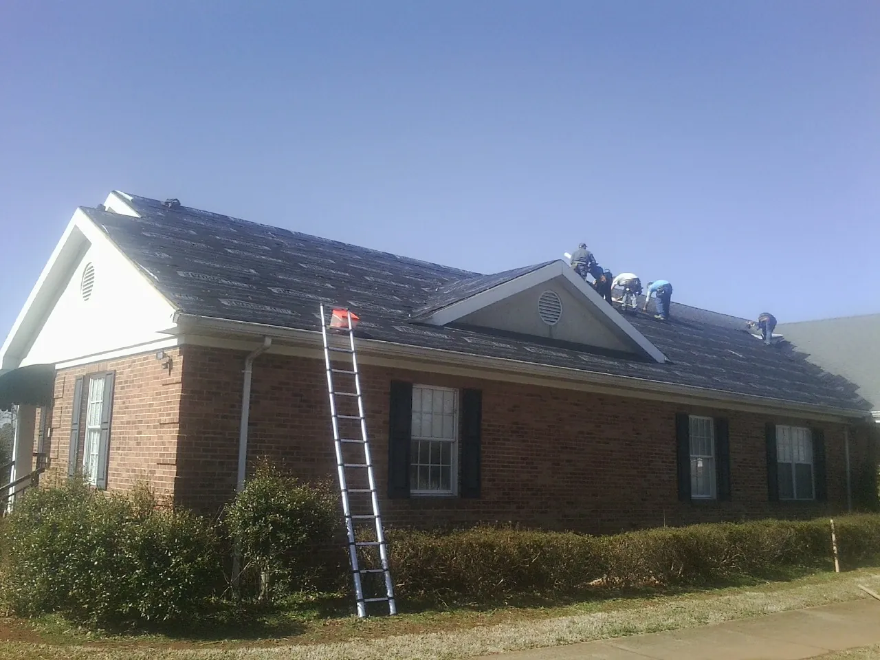 Crew tearing shingles off a brick ranch roof with a ladder set — Emergency Roof Repair work by our crew in Horatio