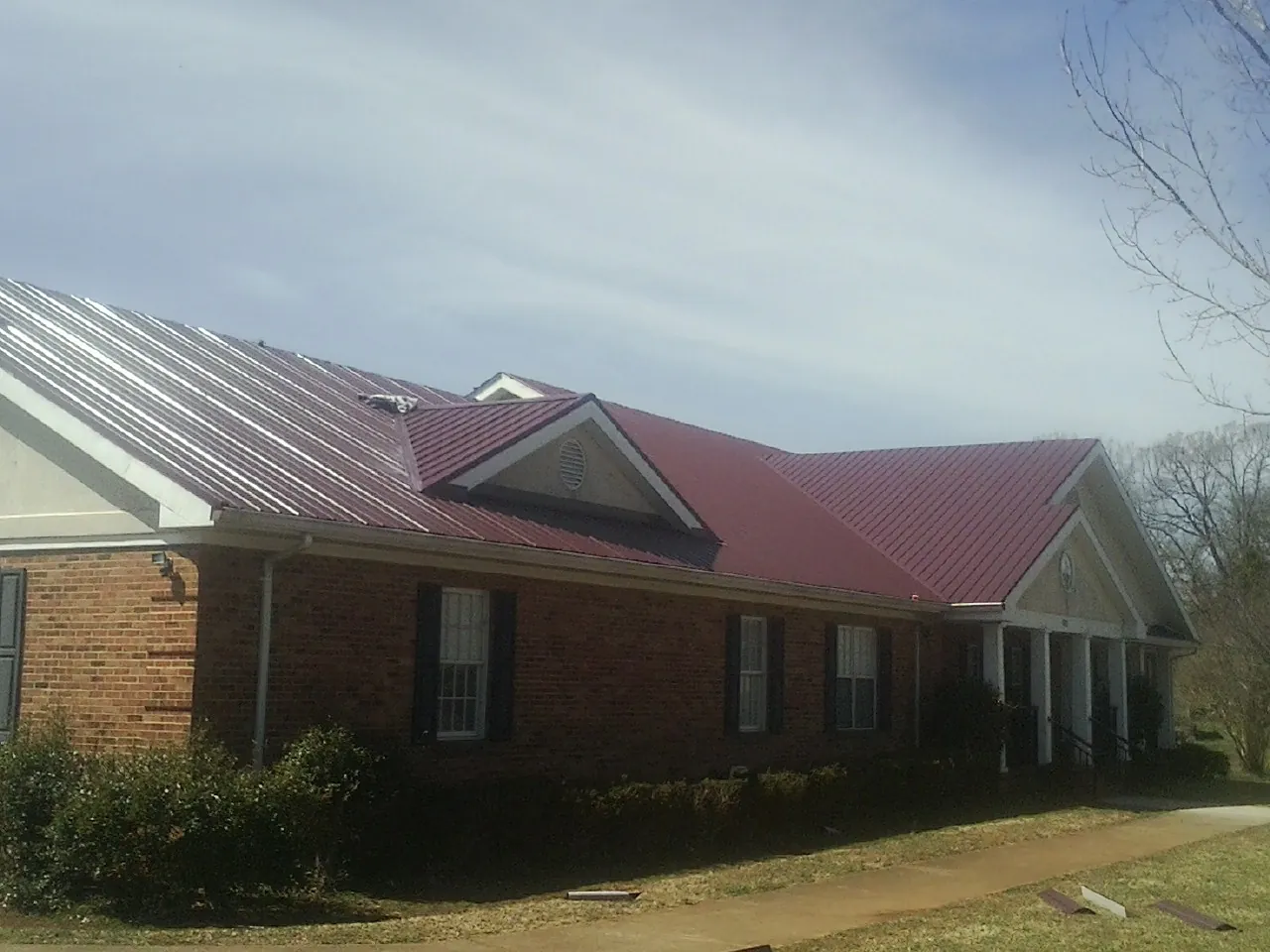 Red metal roof with gabled entries on a long brick building, from a Hail Damage Roof Repair job in Horatio