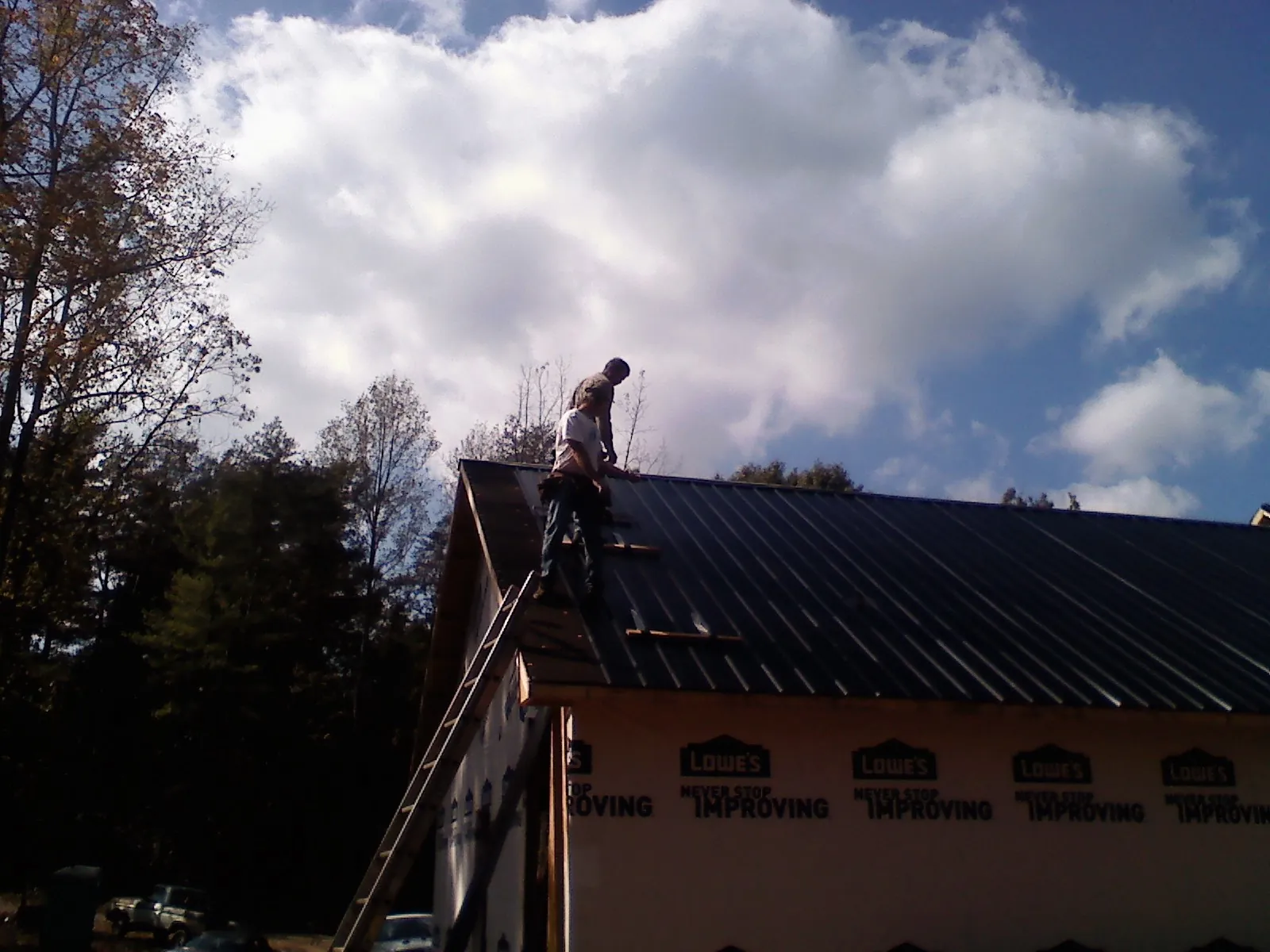 Roofer fastening dark metal panels high against a cloudy sky, from a Roof Inspection job in Horatio