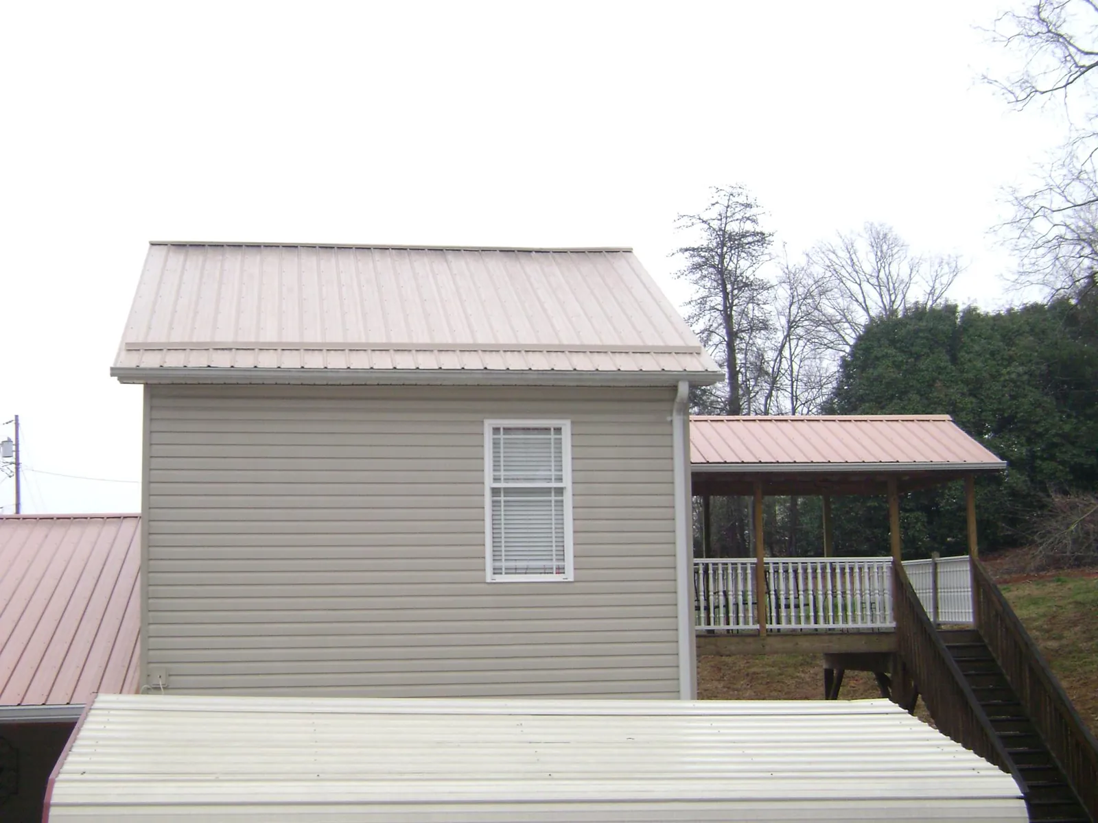 Tan metal roofs on a two story addition and attached porch, from a Roof Replacement job in Horatio